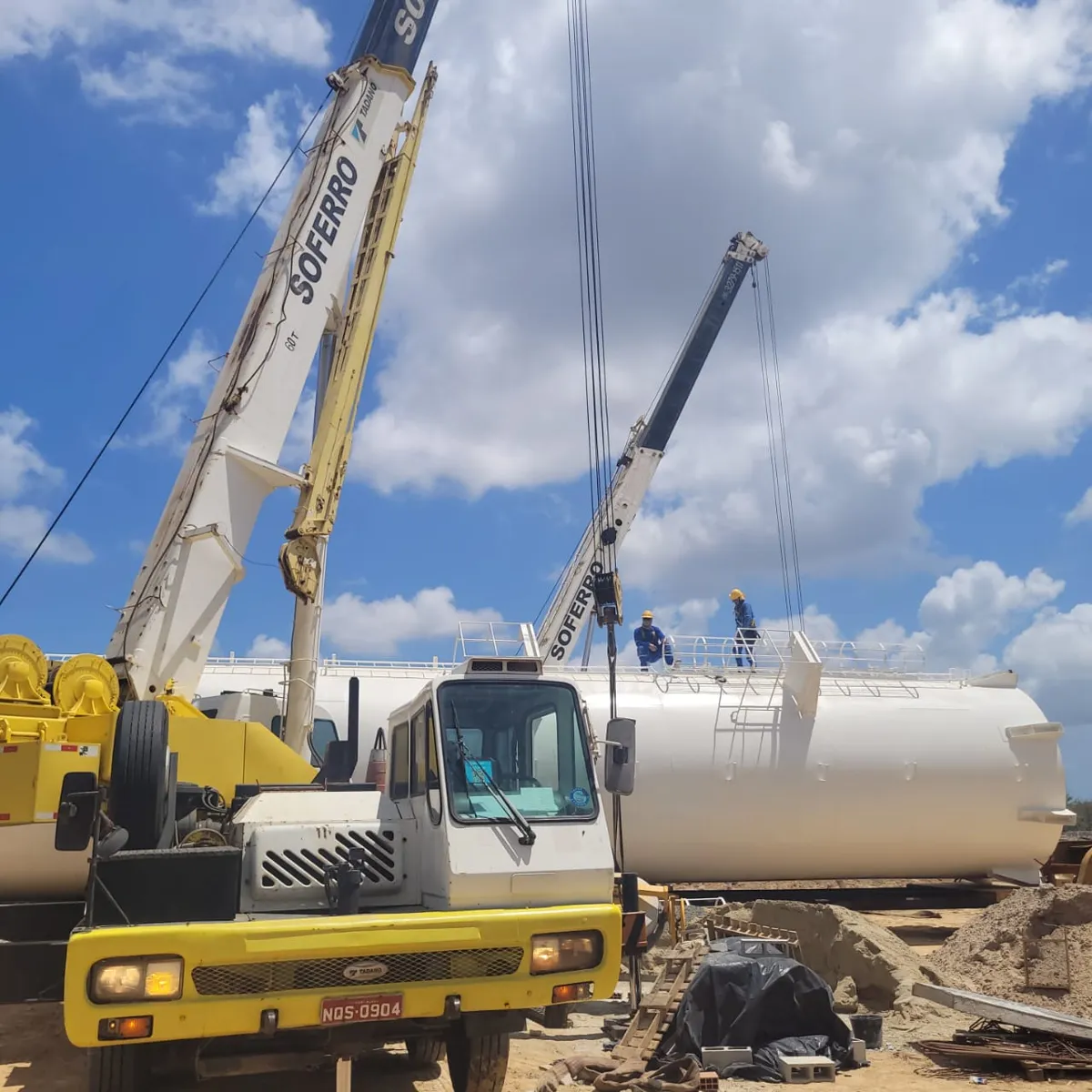 Guindastes içando um tanque metálico em obra da Schuster
