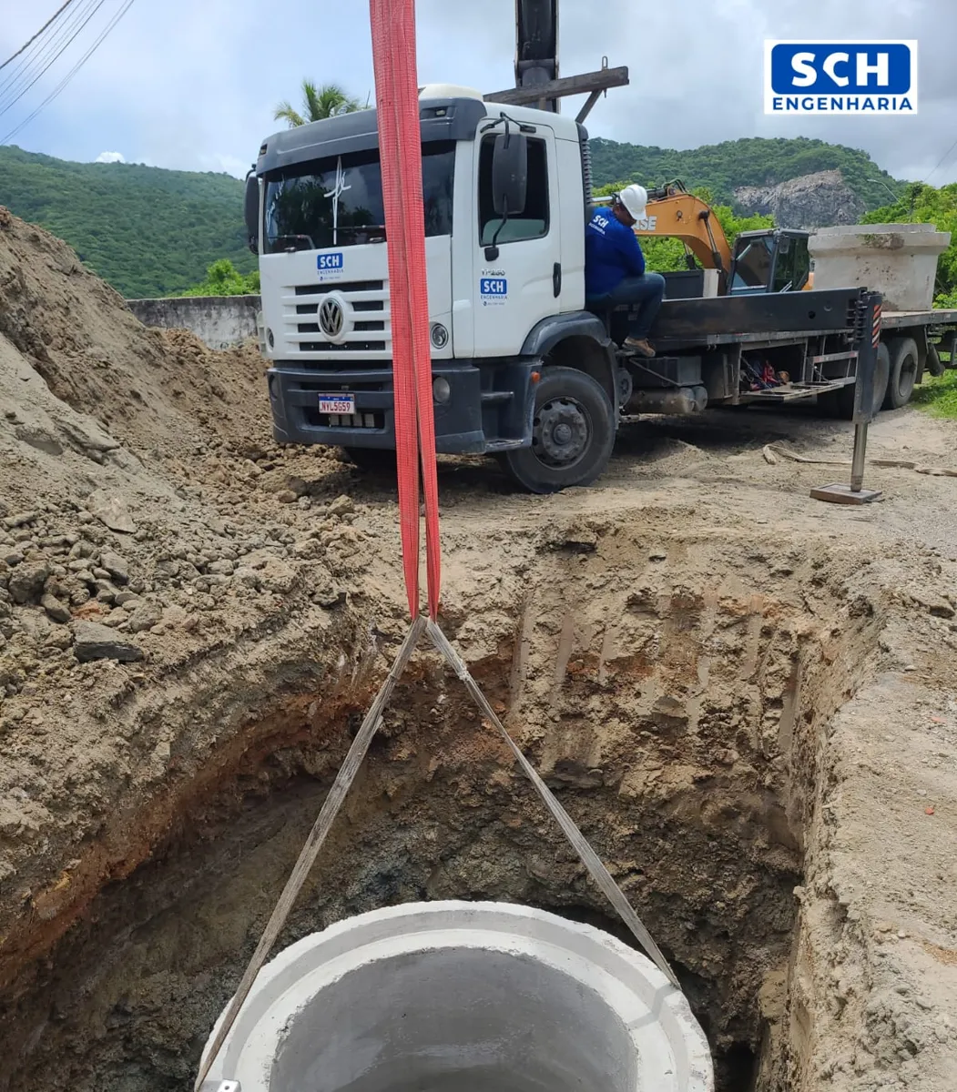 Anel de concreto descendo por guindaste na vala, com caminhão da SCH Engenharia